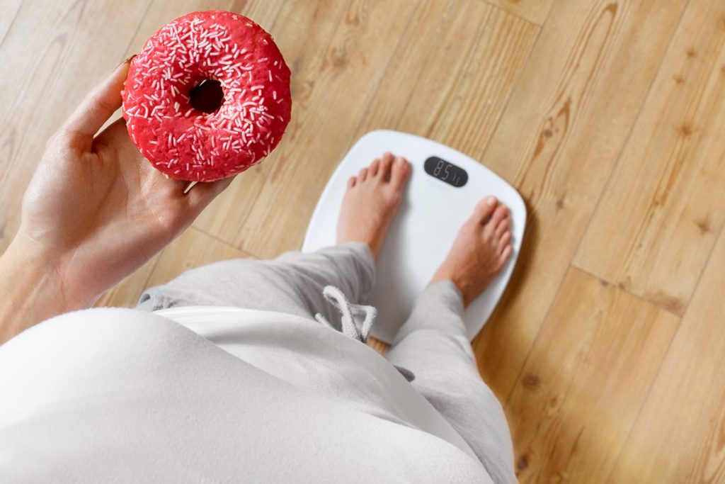 person holding a donut stepping on a scale
