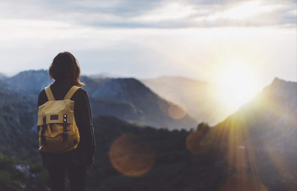 young girl with backpack enjoying sunset on peak of foggy mountain