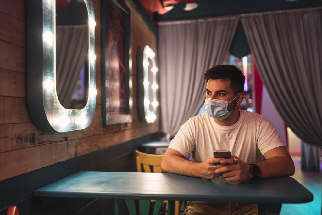 man seated in a table inside a bar while wearing facemask