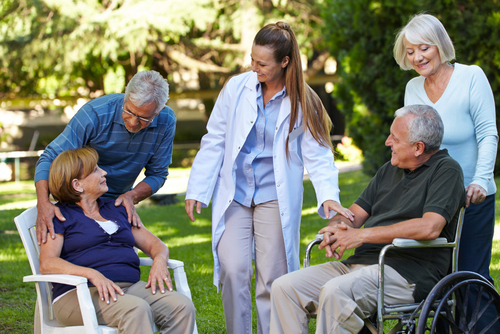 Four senior adults staying the garden of a retirement home with a doctor talking with them.