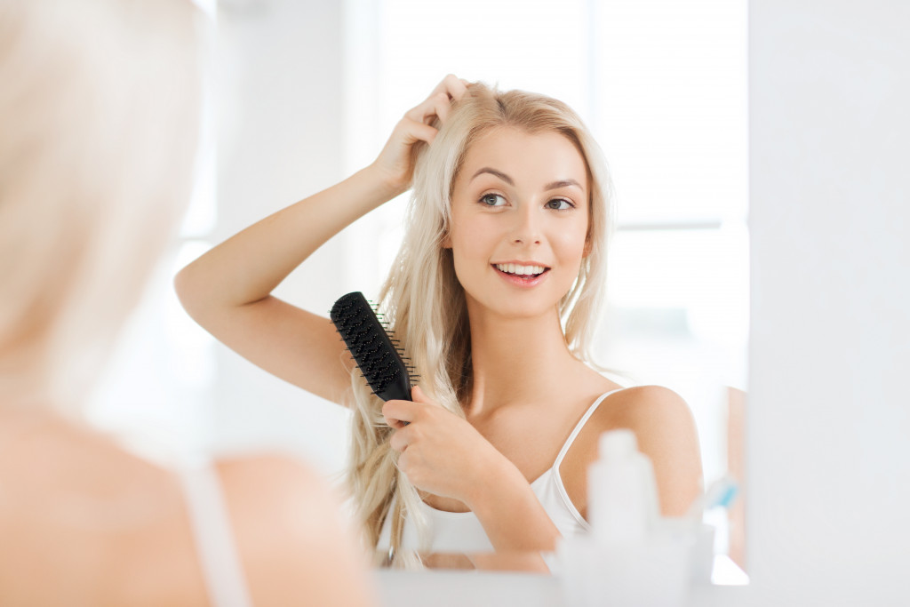 a woman using a hair brush while looking at the mirror