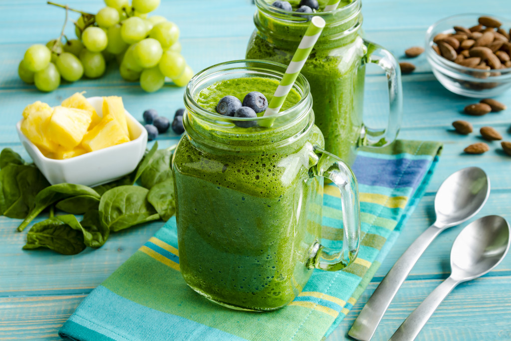 A healthy green smoothie on a table with ingredients and spoons