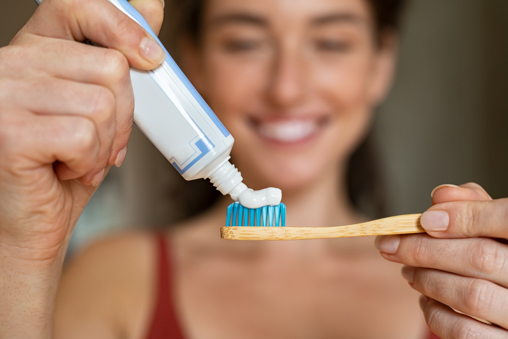 Closeup of girl hands squeezing toothpaste on ecological wooden brush