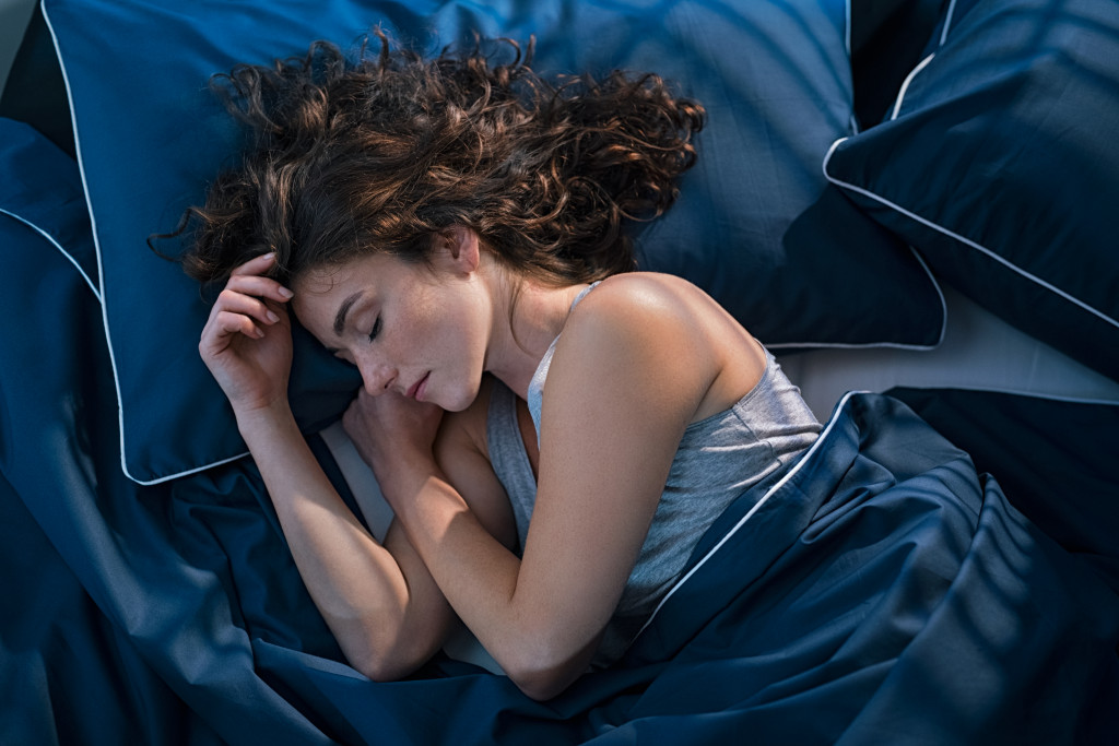 Young woman sleeping in bed with a blue blanket.