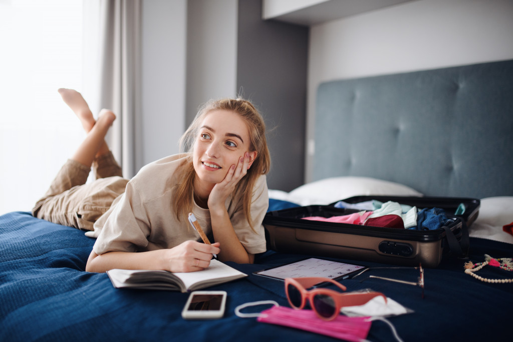 woman thinking about what to pack with notebook and phone in bed