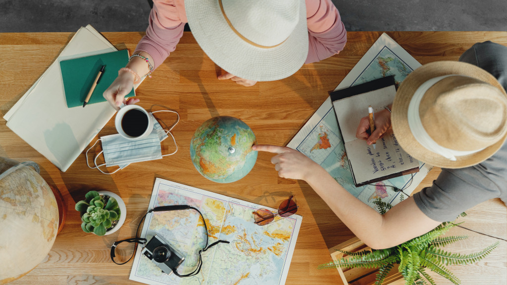 two people planning vacation while pointing at mini globe and maps in table