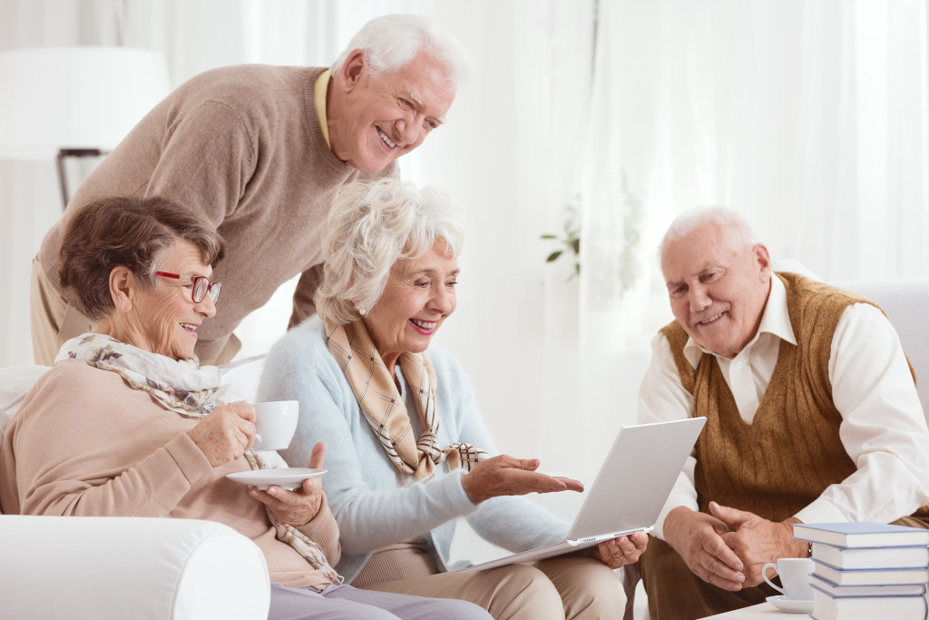 Senior adults socializing in a living area while using a laptop.