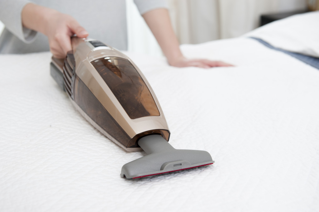 A person using a hand vacuum on a white bed