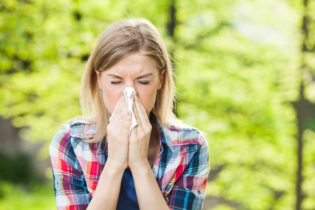 A woman covering her mouth and nose while sneezing outdoors