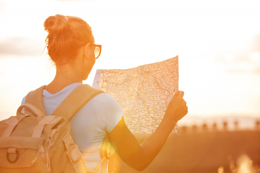 woman with sunglasses holding map and looking ahead at her destination in sunset