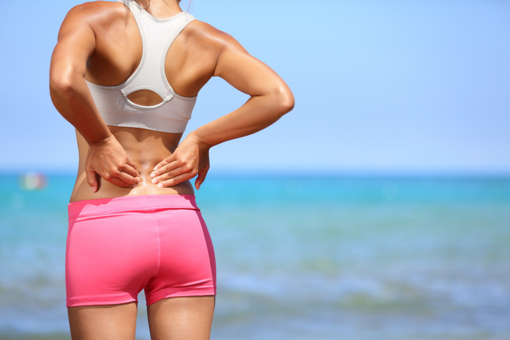 woman standing in beach shore holding back representing body pain