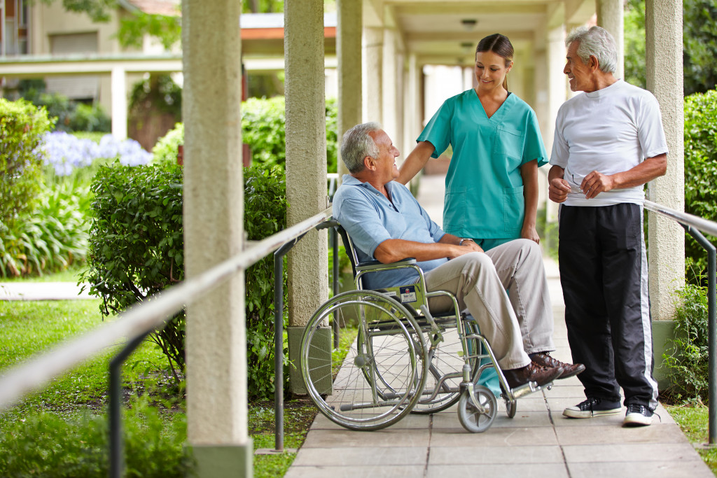 elderly disabled man walking at the hallway with his personal nurse and wife