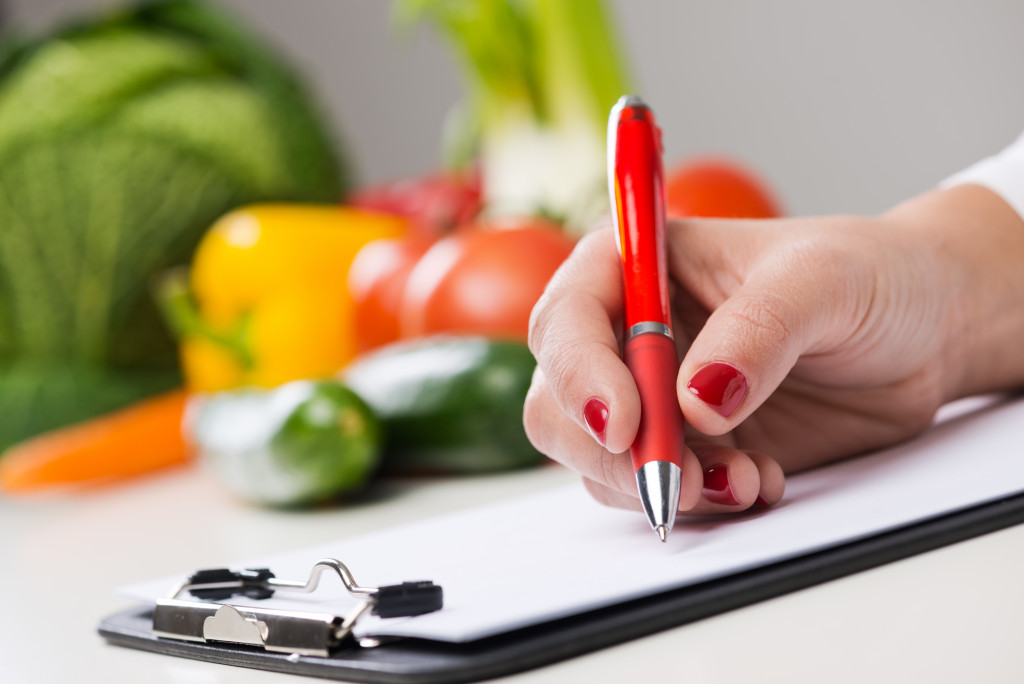 woman writing on a clipboard with vegetables at the back