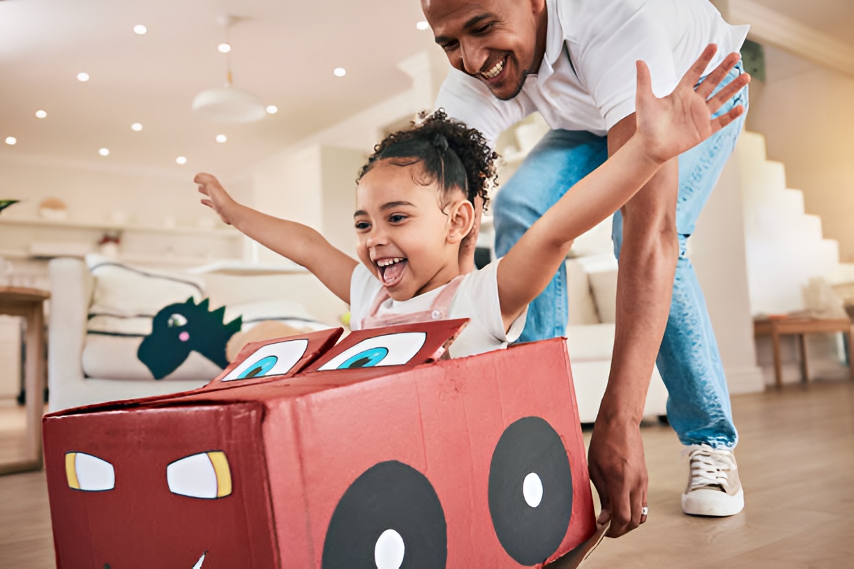 father playing with his daughter in a cardboard car